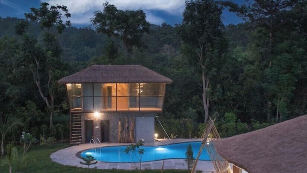 Una villa moderna con piscina, rodeada de exuberante vegetación y un paisaje boscoso.