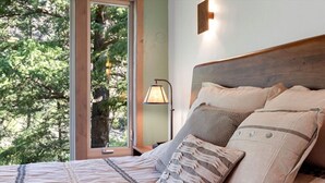 A bedroom with a large window, a bed with beige bedding, and a nightstand with a lamp. - * * *Waters Edge Lodge* **************** (Bonner-West Riverside)