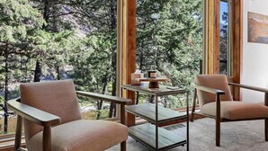 A room with two beige armchairs, a small wooden table, and a view of a forest through large windows. - * * *Waters Edge Lodge* **************** (Bonner-West Riverside)
