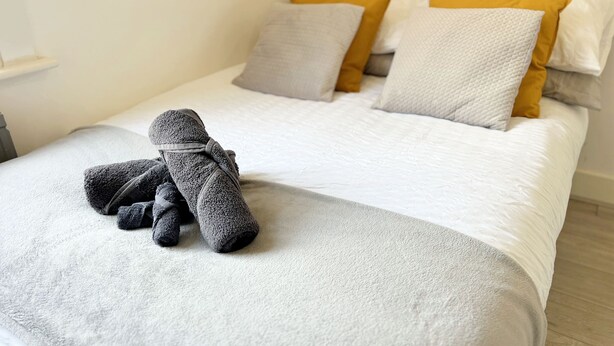 A neatly made bed with a gray towel and a white blanket. - Minet Gardens Central-Suite 3 (London)