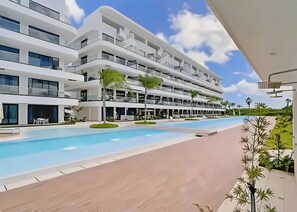 A modern multi-story hotel with a swimming pool, outdoor seating, and a clear sky.