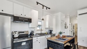 Une cuisine moderne dotée d’appareils électroménagers en acier inoxydable, de meubles blancs et d’un îlot central avec des tabourets.