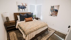 Une chambre à coucher avec un lit, des tables de chevet, une lampe et des œuvres d’art accrochées aux murs.