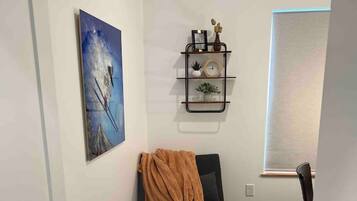 A room with a black sofa, a patterned rug, a wall-mounted shelf with decorative items, and a framed picture.