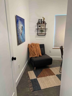 Une pièce avec un canapé noir, un tapis à motifs, une étagère murale ornée d’objets décoratifs et un tableau encadré.