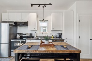 Una cocina moderna con armarios blancos, una isla central con encimera rústica y una lámpara colgante.