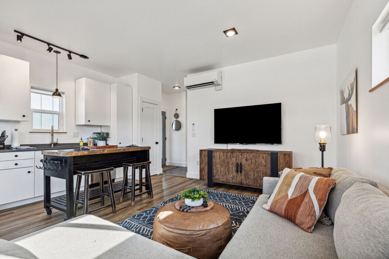 A modern living space with a kitchen, dining area, and a seating area with a sofa and ottoman.