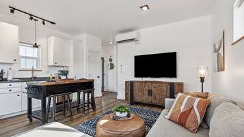 A modern living space with a kitchen, dining area, and a seating area with a sofa and ottoman.