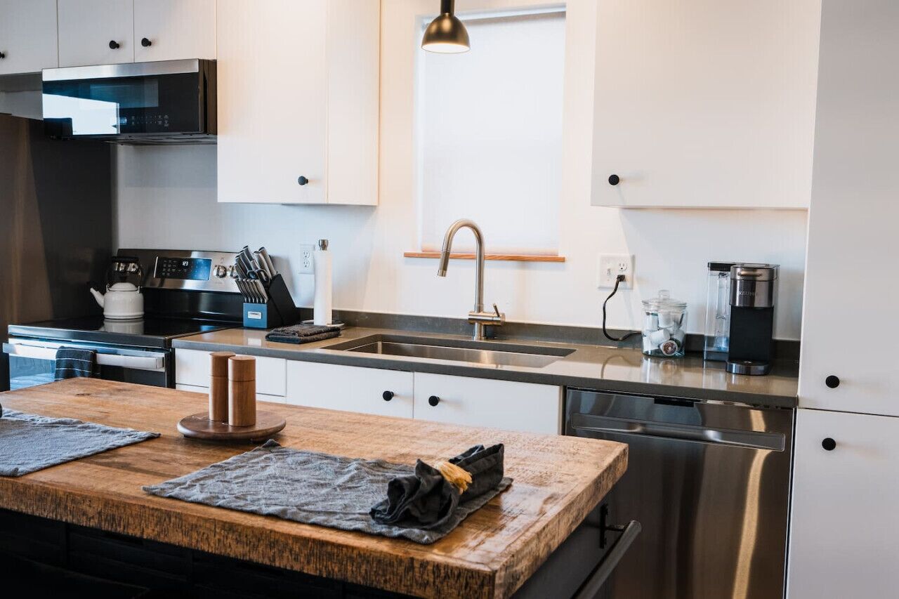 A modern kitchen with stainless steel appliances, a wooden countertop, and a hanging pendant light.