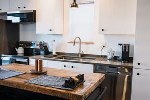 Una cocina moderna con electrodomésticos de acero inoxidable, una encimera de madera y una lámpara colgante.
