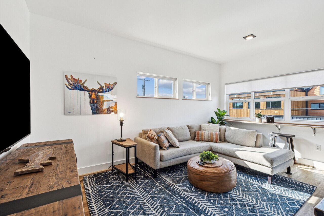 A modern living room with a sectional sofa, a coffee table, a rug, and a wall-mounted TV.