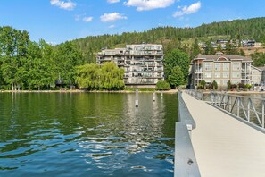 Een hotel aan het water met meerdere balkons, een steiger en een beboste heuvel op de achtergrond.
