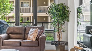 A modern living room with a brown leather sofa, a large potted plant, and a sign that reads "At the Lake we forget to count the days."