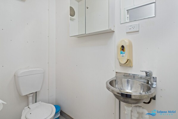 A bathroom with a toilet, a hand dryer, a sink, and a mirror. - Hive Hotel  (Moruya)