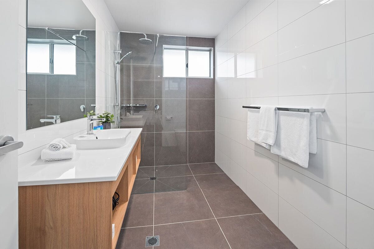 A modern bathroom with a large mirror, two sinks, a shower area, and a towel rack.