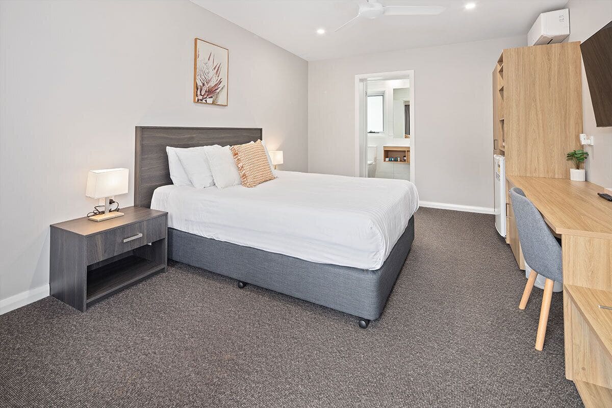 A modern hotel room with a large bed, a desk, and a wardrobe.