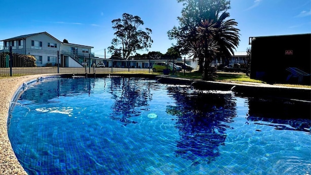 Una piscina con agua azul cristalina, rodeada por una valla y un edificio al fondo.