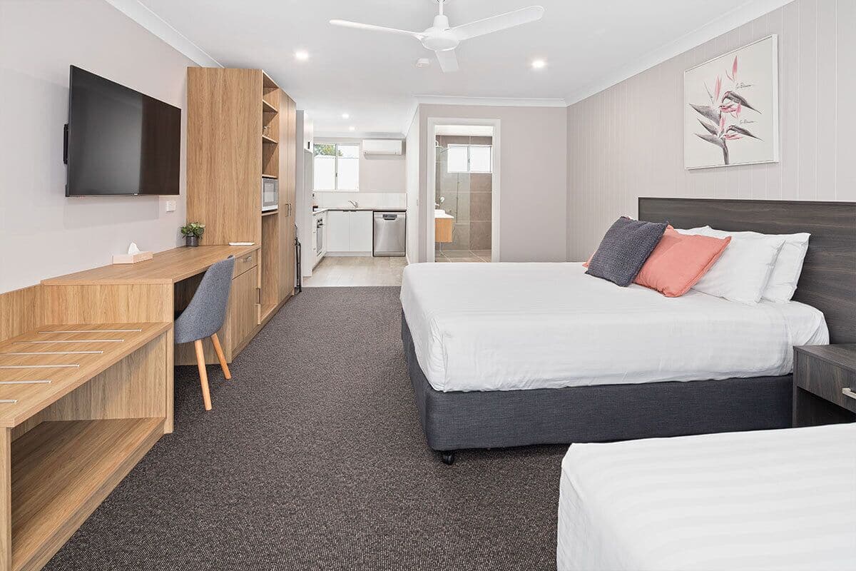 A modern hotel room with a large bed, a desk, a chair, a TV, and a shower area.