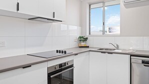 Una cocina moderna con armarios blancos, horno empotrado, lavavajillas y ventana con vistas al exterior.