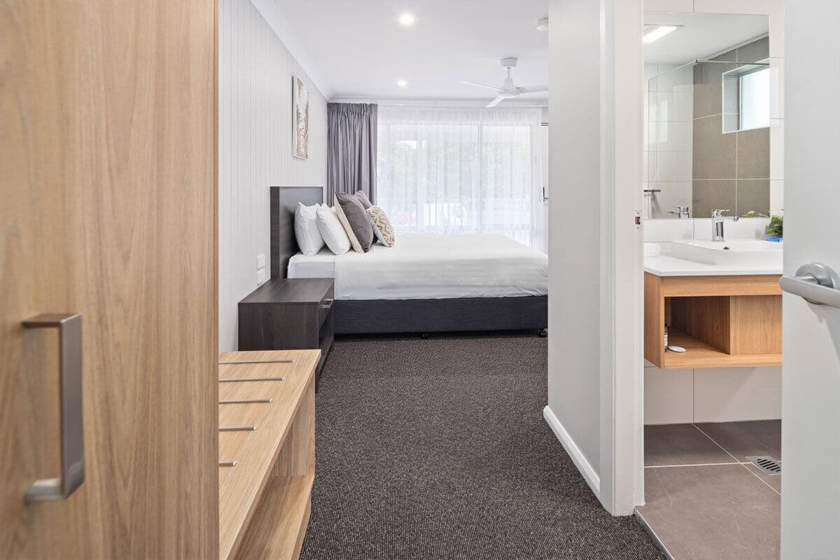 A modern hotel room with a bed, bedside table, and a bathroom with a sink and mirror.