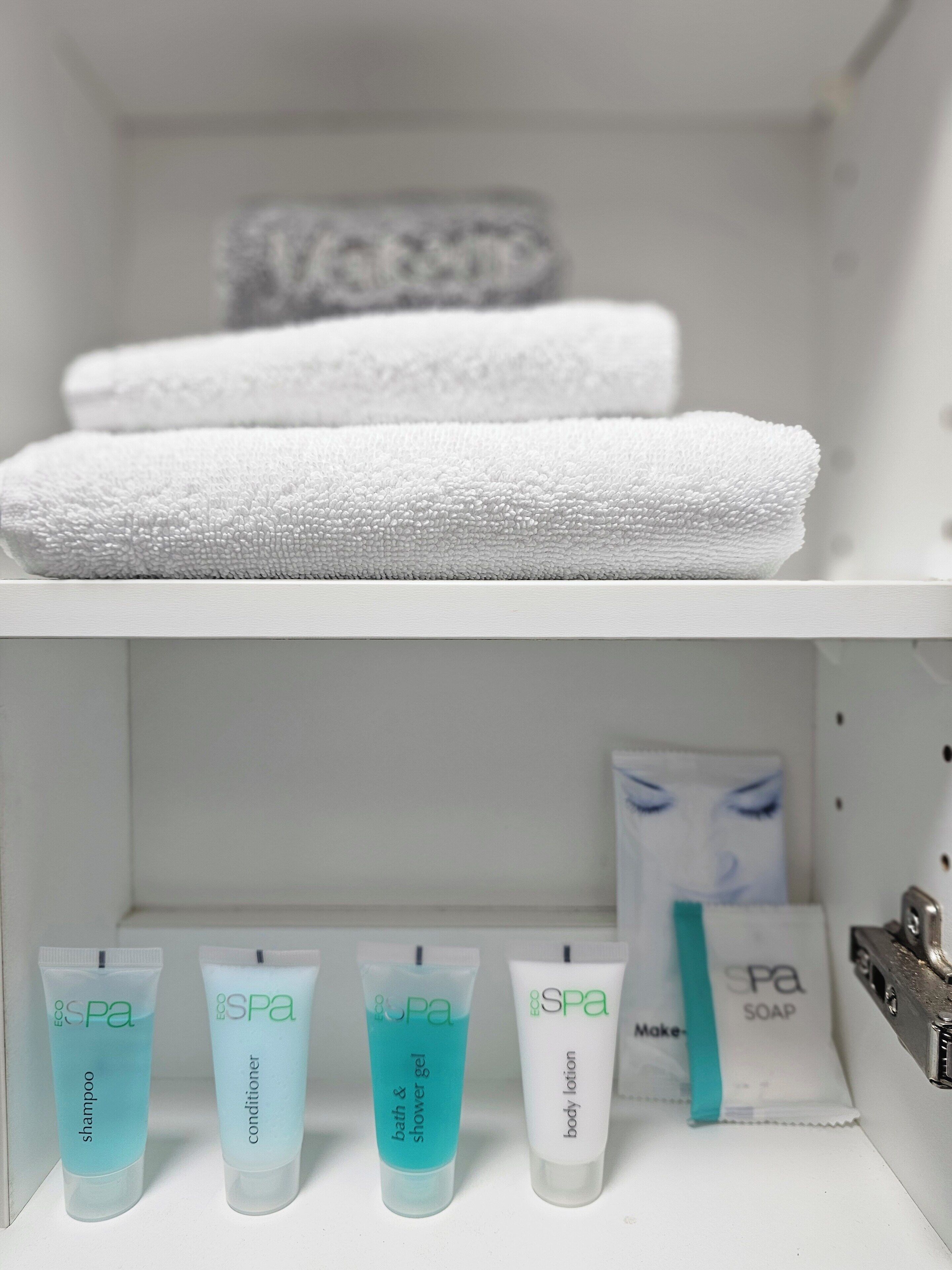 Un baño con toallas blancas apiladas en un estante y diversos productos de spa en el estante inferior.