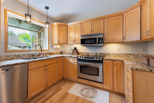 A modern kitchen with wooden cabinets, stainless steel appliances, a granite countertop, and a window with a plant.