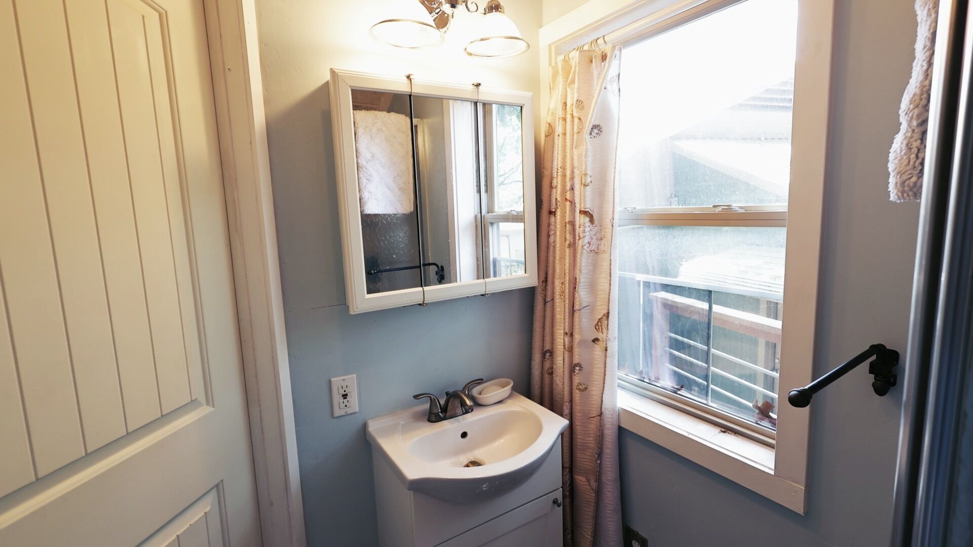 Een badkamer met een witte wastafel, een spiegel en een raam met gordijnen.