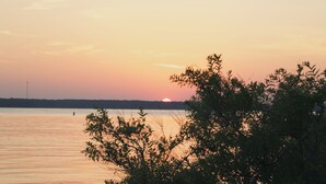 A sunset over a calm body of water with a distant shoreline and some vegetation in the foreground. - Romantic guest house within walking distance from Lake Texoma. (Pottsboro)