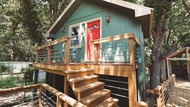 A wooden deck with a red door, a small porch with a railing, and a staircase leading up to the door. - Romantic guest house within walking distance from Lake Texoma. (Pottsboro)