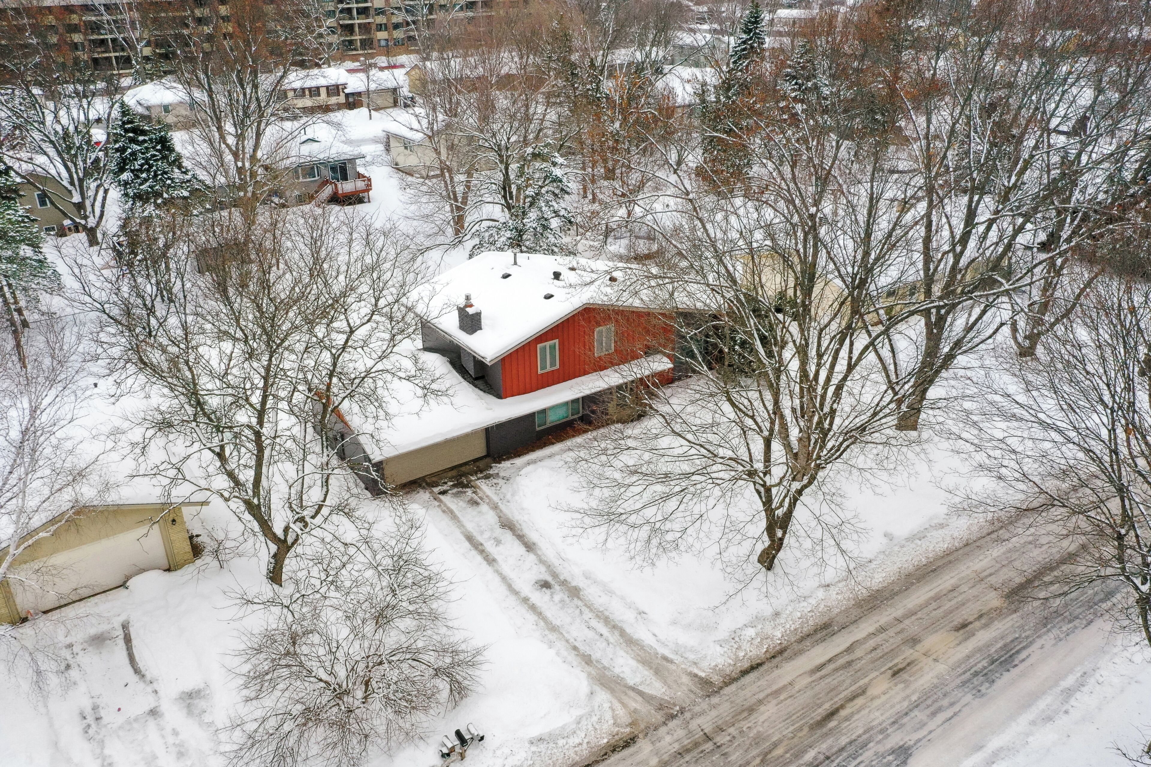 A red house with a snow-covered roof, surrounded by leafless trees and a snow-covered ground.