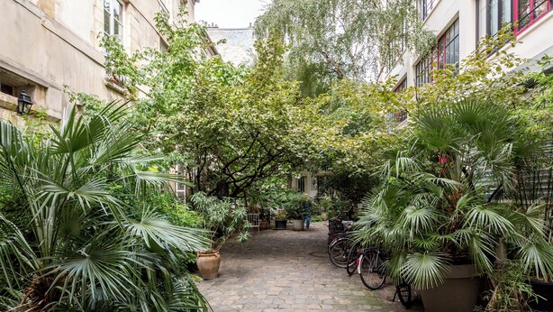 A cobblestone courtyard with potted plants, bicycles, and a person walking. - Merveil - Family Suite - Marais - Fbg St Antoine (Paris)