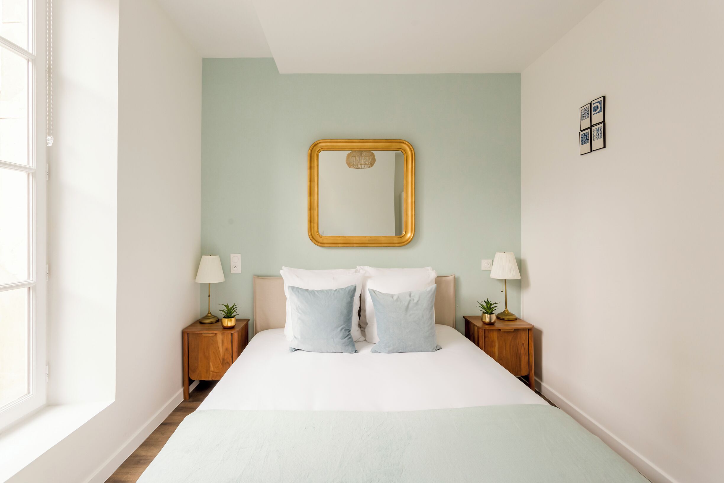 Une chambre à coucher avec un lit, deux tables de chevet avec des lampes, un miroir au mur et une fenêtre.