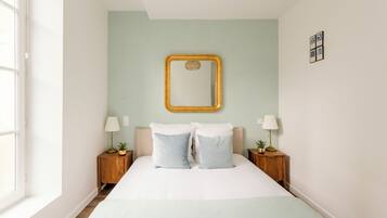 Une chambre à coucher avec un lit, deux tables de chevet avec des lampes, un miroir au mur et une fenêtre.