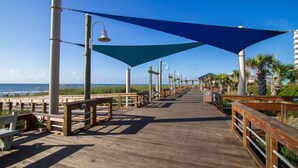 A wooden boardwalk with benches and shaded areas, leading towards the ocean. - Anchor Down - Ocean & Canal Views, Near Beach Access, CB Pier, Freeman Park, Outdoor Space, Grill (Carolina Beach)