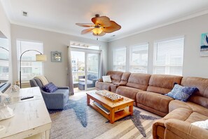 A spacious living room with a brown leather sofa, a wooden coffee table, and a ceiling fan.