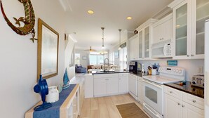 A modern kitchen with white cabinetry, a central island, and a dining area in the background. - Anchor Down - Ocean & Canal Views, Near Beach Access, CB Pier, Freeman Park, Outdoor Space, Grill (Carolina Beach)