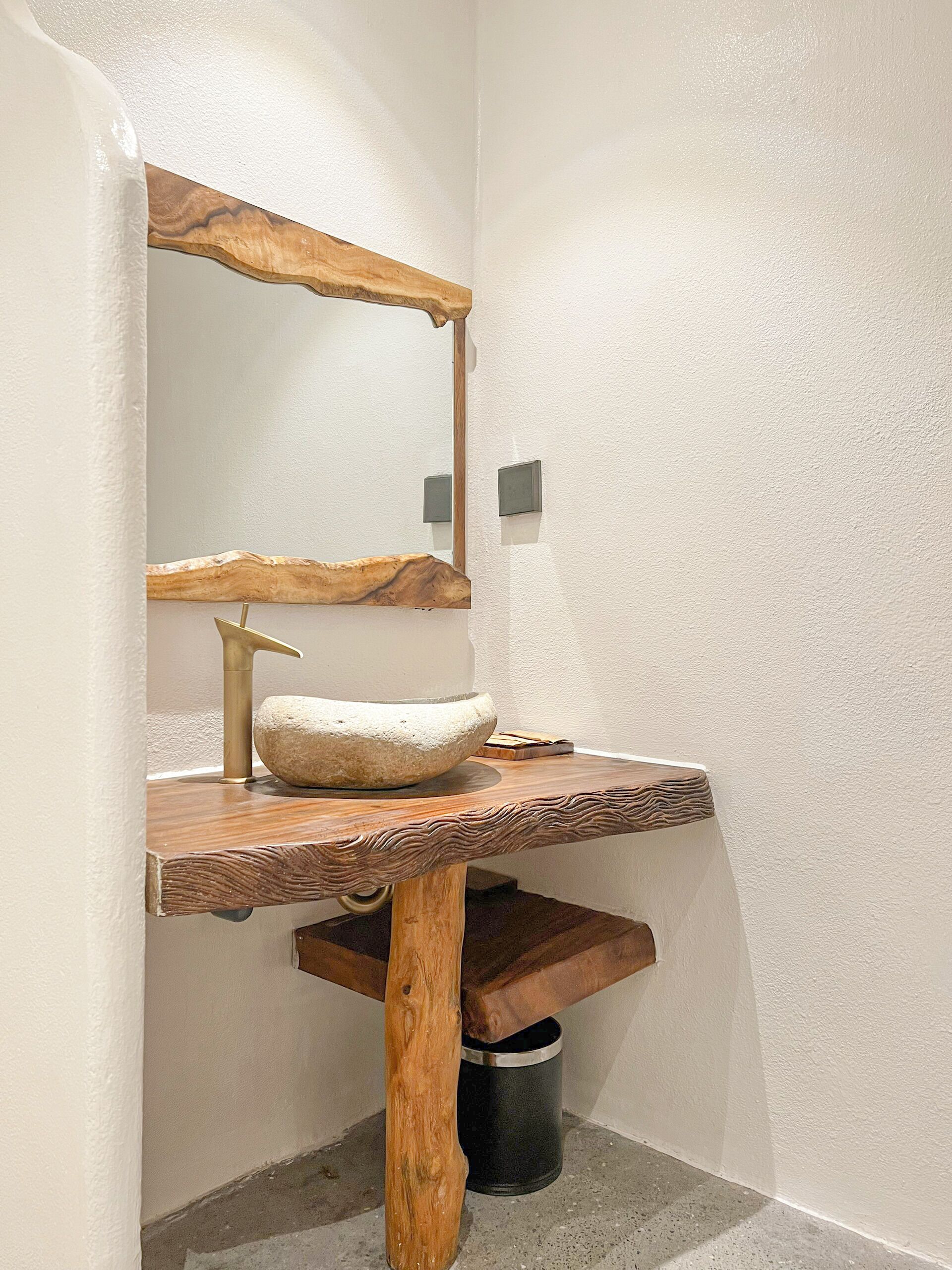 A bathroom with a rustic wooden vanity, a stone sink, and a wall-mounted mirror.