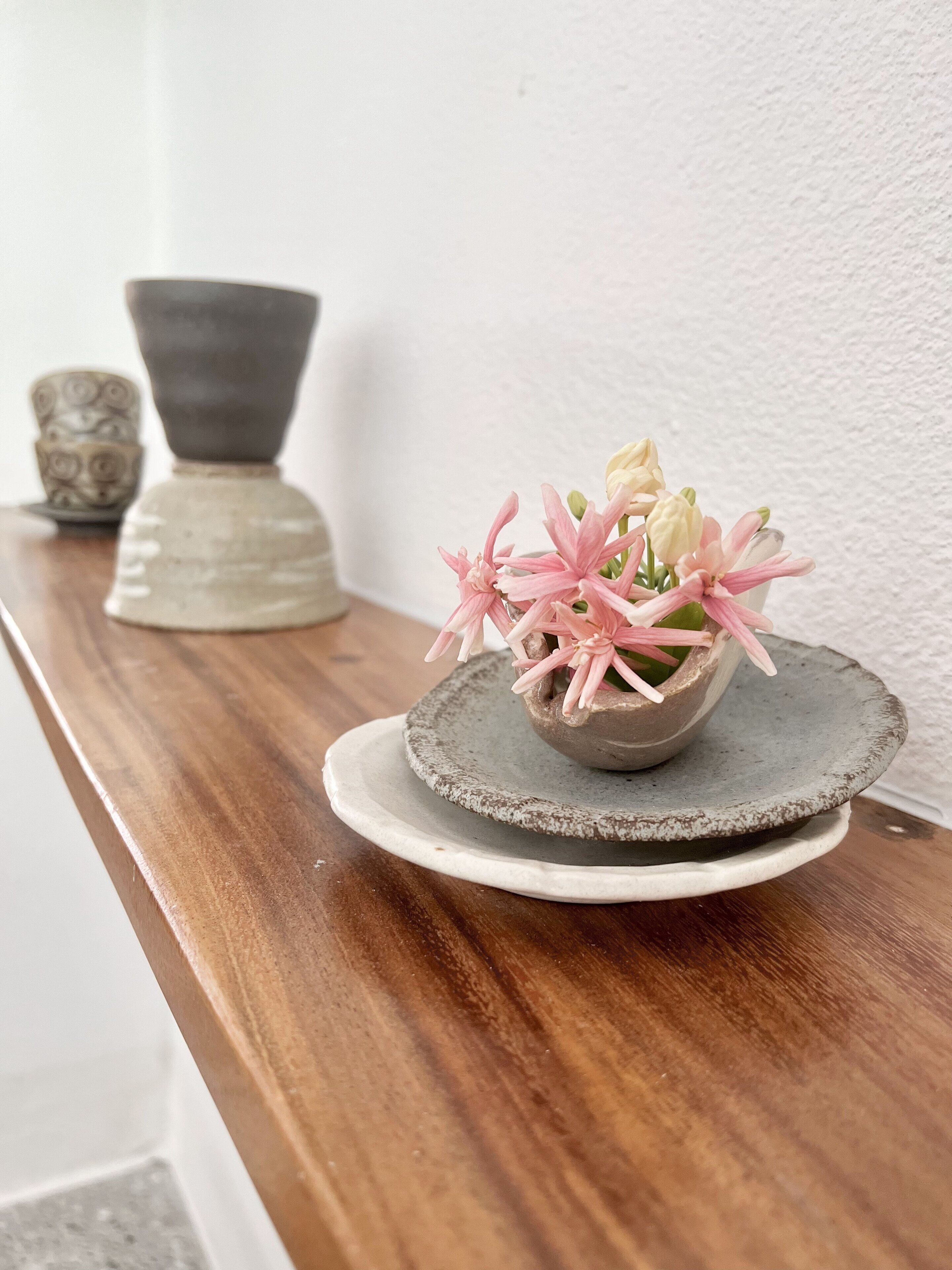 Una repisa de madera con un cuenco de cerámica que contiene flores rosas, un plato de cerámica y un cuenco decorativo.