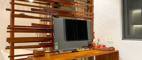 Ein TV-Schrank aus Holz mit einem Flachbildfernseher, einem gewebten Korb und einem kleinen Tisch mit Flaschen und einer Fernbedienung.
