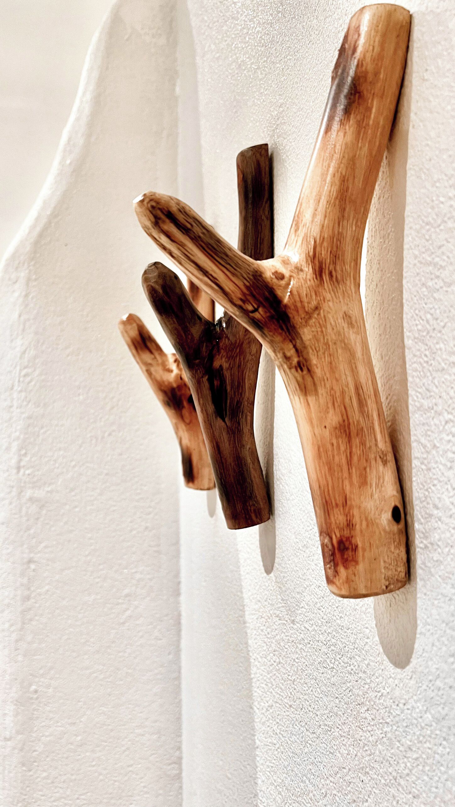 Un perchero de madera con tres ganchos frente a una pared blanca con textura.