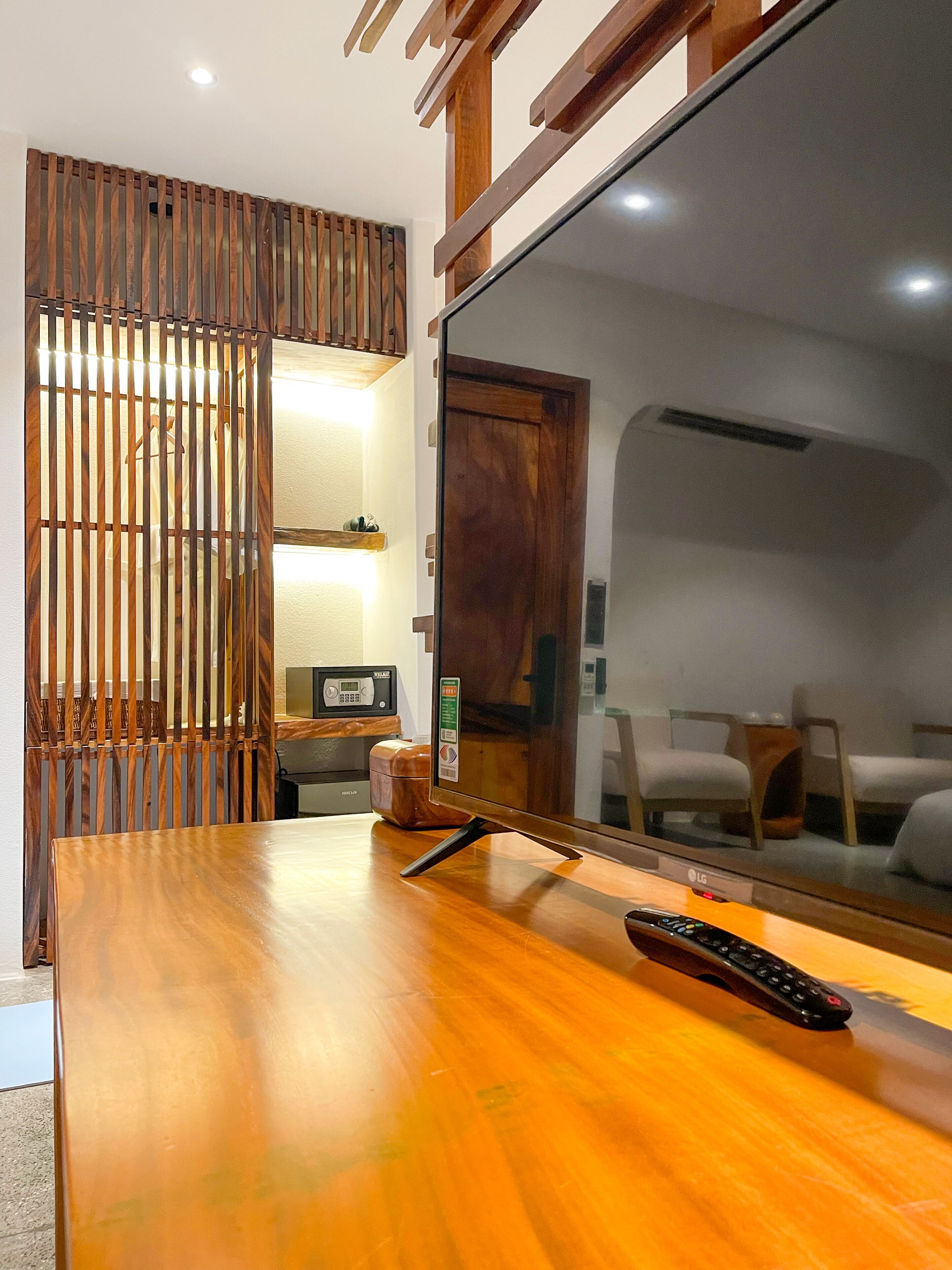 A wooden desk with a large mirror, a remote control, and a microwave in the background.