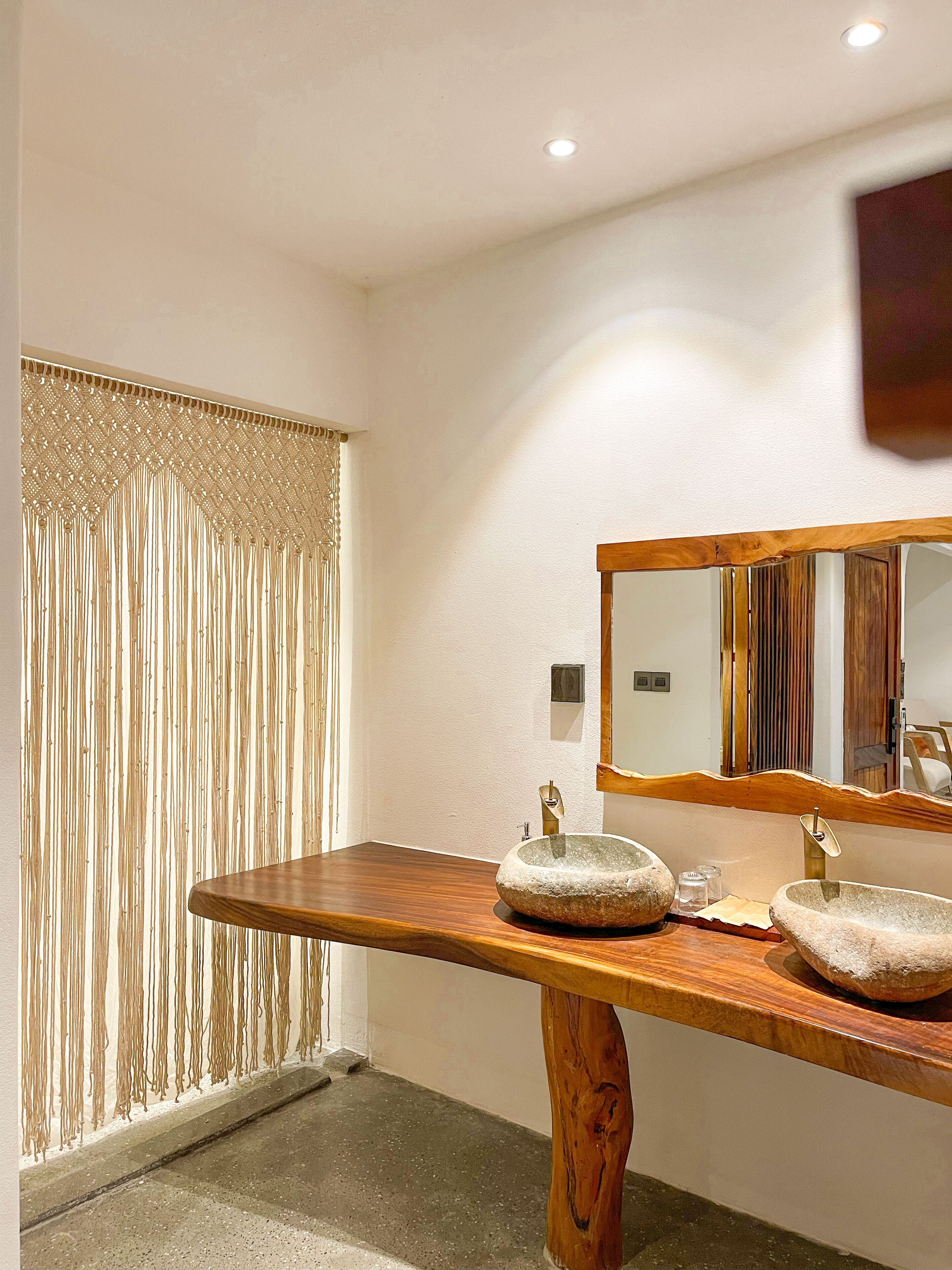 A bathroom with a wooden vanity, two stone sinks, a mirror, and a textured curtain.