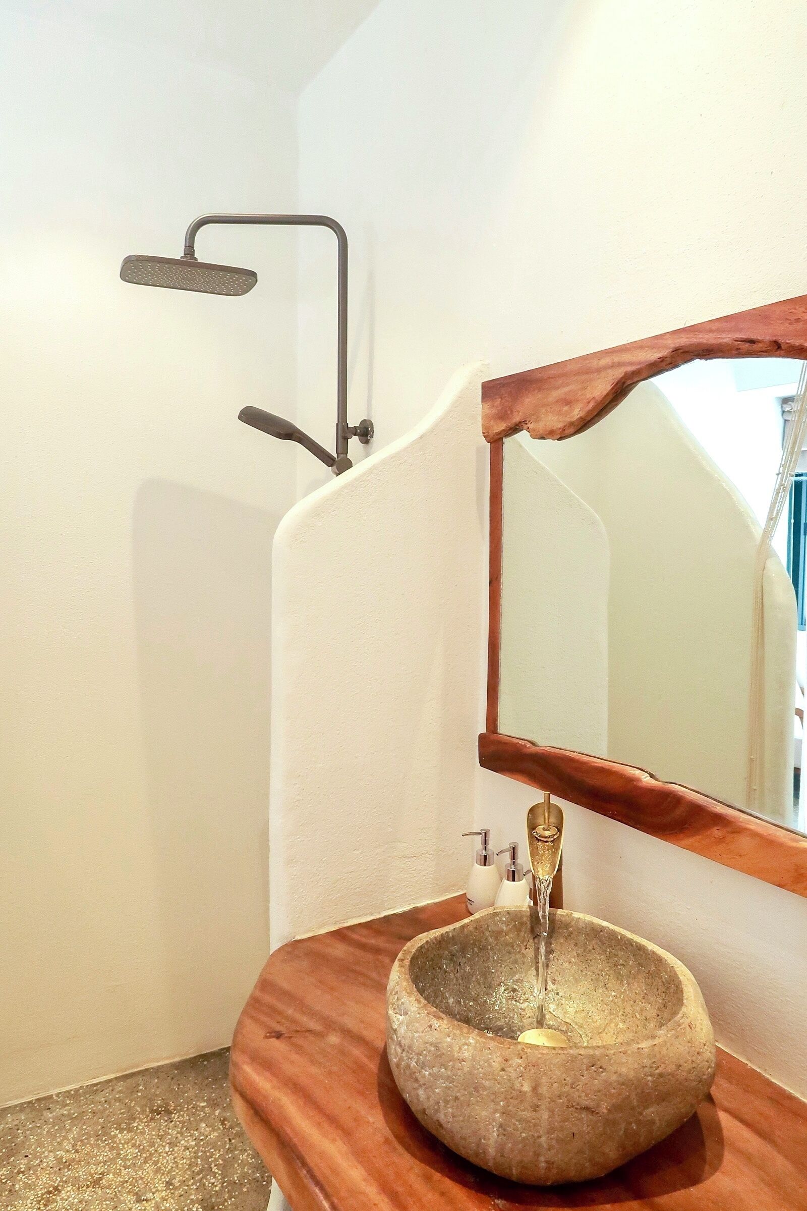 Ein Badezimmer mit einem Steinkonstruktion-Waschbecken, einer Holz-Kommode, einem Spiegel und einem an der Wand befestigten Duschkopf.
