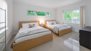 Una habitación de hotel moderna con dos camas, un escritorio pequeño y vistas a zonas verdes a través de las ventanas.