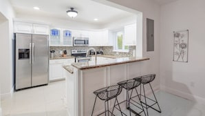 Una cocina moderna con armarios blancos, electrodomésticos de acero inoxidable, encimera de granito y una zona de bar con taburetes metálicos.
