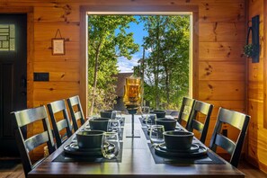 Une table de salle à manger en bois, mise avec des assiettes, des bols et des verres, entourée de chaises.