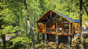 A wooden cabin with a balcony, surrounded by trees.