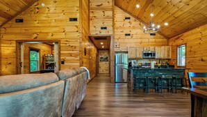 A log cabin interior with a sofa, kitchen, and dining area.