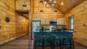 A wooden cabin interior with a kitchen area, bar stools, and a stone countertop.