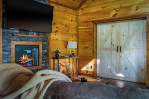 Une pièce chaleureuse avec une cheminée, un téléviseur fixé au mur et une grande porte en bois.